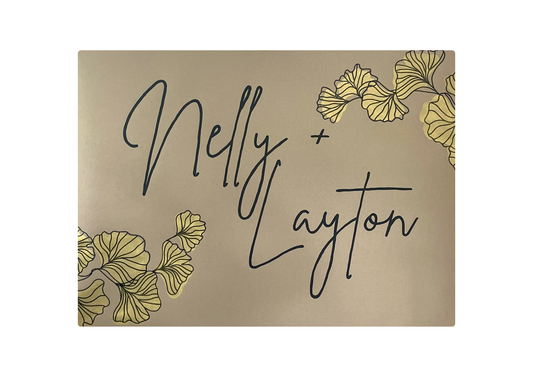 Card with 'Nelly + Layton' text and gold leaf designs on a beige background